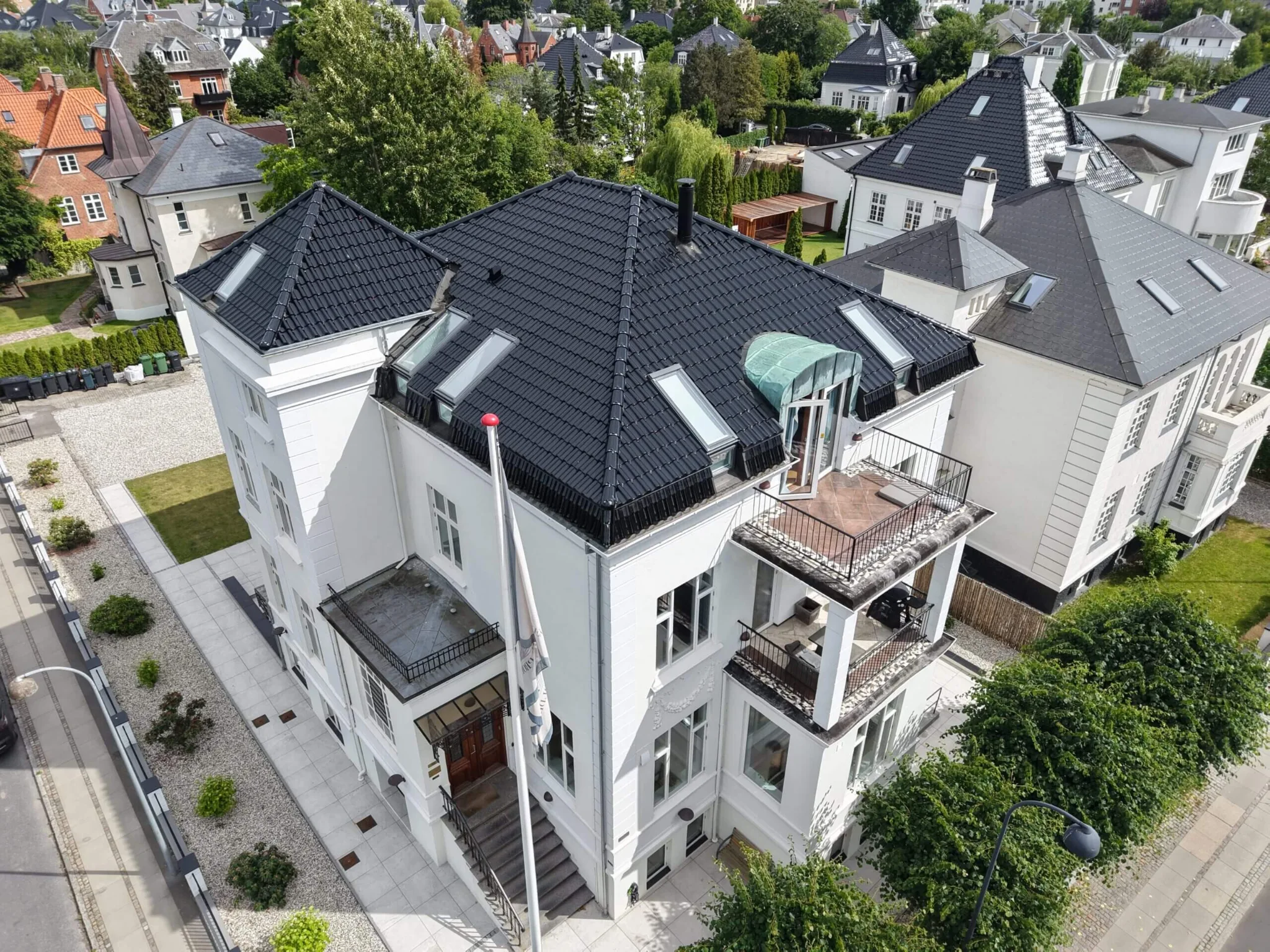 Hvid ejendom med tegltag og grønne omgivelser set fra oven
